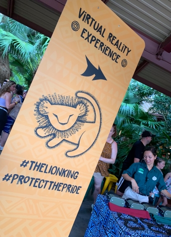There is a tall yellow sign with a black arrow facing right. It reads "Virtual Reality Experience" and has a cartoon sketch of a lion.
