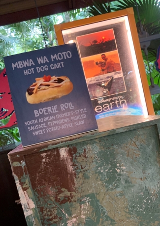 There is a faded green bin. Atop is a sign that shows a picture of the Boerie Roll