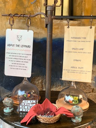 This is the display for the Leopard booth. There are two dishes displayed under glass covers, silverware, and napkins. There is also a sign that lists each dish.