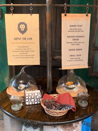 This is the display for the Lion station. There are two dishes displayed under glass covers. There is a sign listing each dish. There is also napkins and silverware.