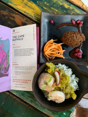 There are two dishes. One has a fried brown fritter with a few shredded carrots and surrounded by a purple pomegranate sauce and some pomegranate seeds. The second bowl has white rice with a thick bright green sauce, topped with two booked shrimp and a shred of radish.